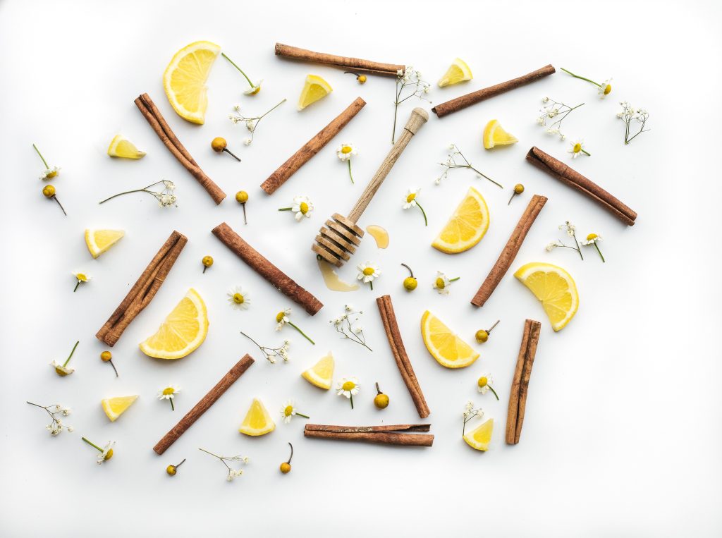 Cannelle, citron, miel et fleurs vus de haut sur une table blanche