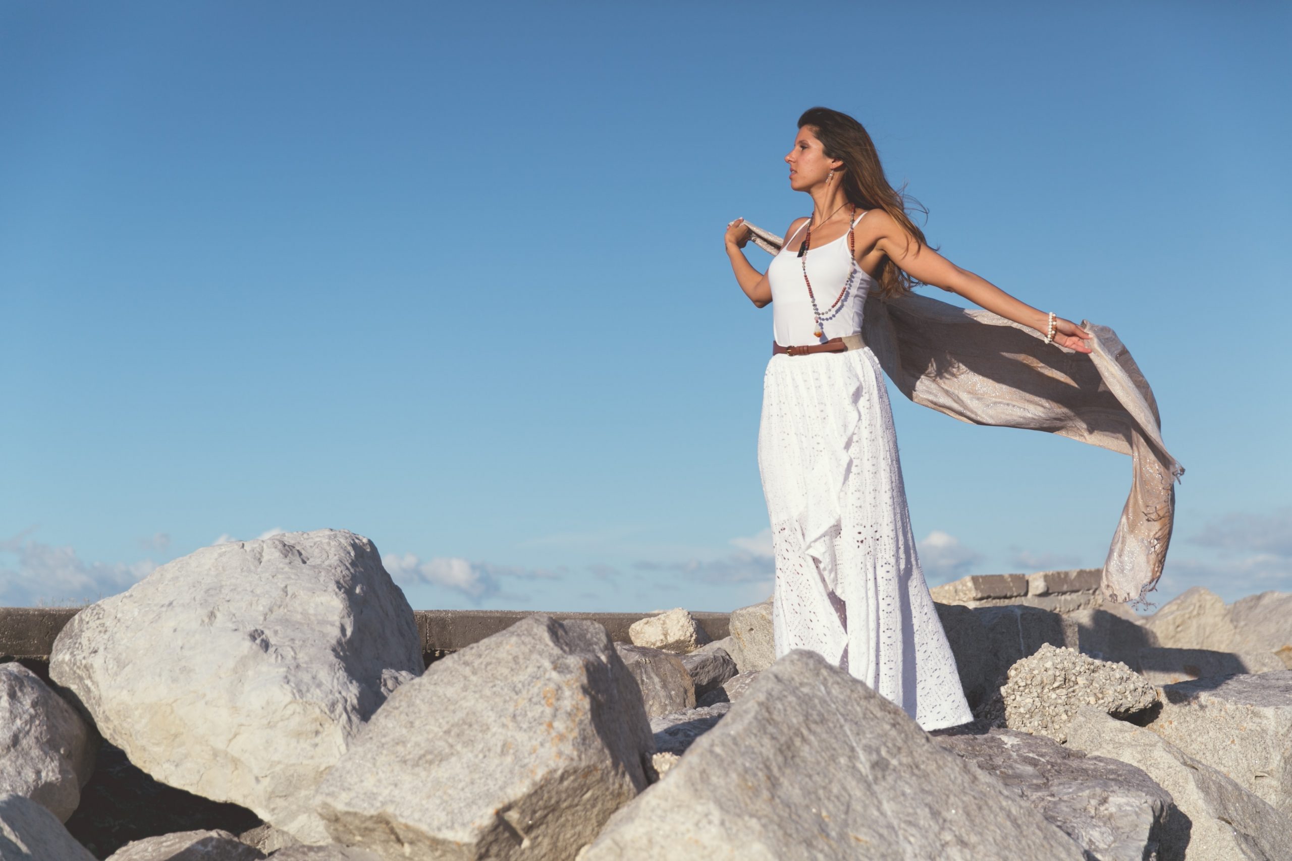 femme sur des rochers portant un robe longue blanche et tenant un foulard