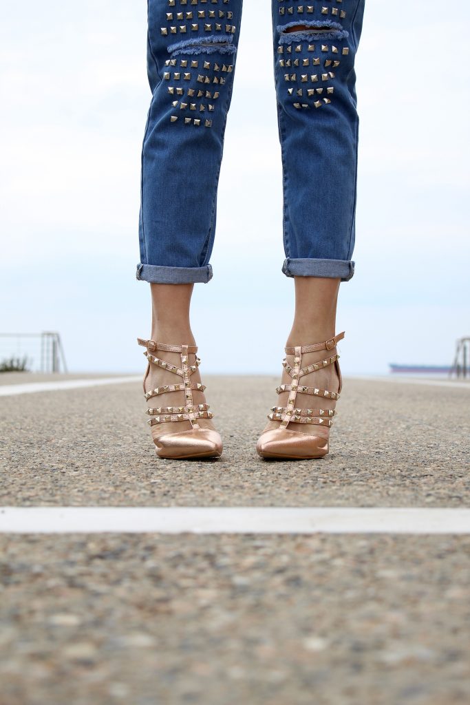 zoom sur les jambes d'une femme portant un jean avec des clous et des chaussures à talons claires avec des clous