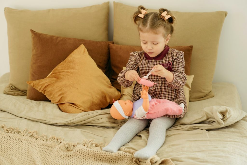 petite fille assise sur un lit qui donne à manger à sa poupée